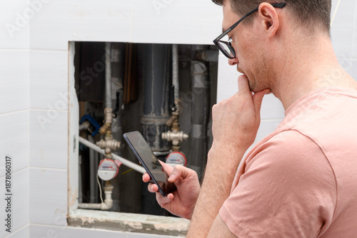 Obraz na plátně Man reviews repair estimate on smartphone beside open plumbing hatch with water meters, worries about leak damage and service cost