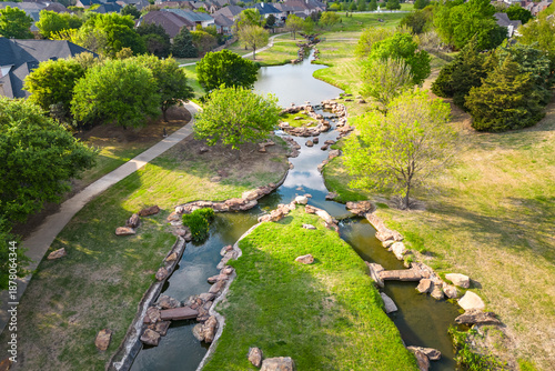 Aerial view of park waterway winding through green space with trees grass and pedestrian paths