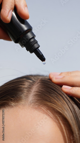 Woman applying hair serum to her scalp for healthy hair growth and nourishment