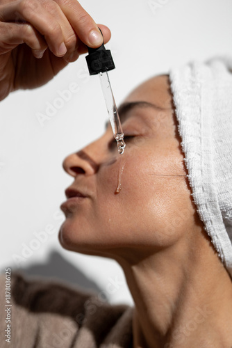 Картината върху платно Side profile close-up of adult woman applying hydrating facial serum with glass