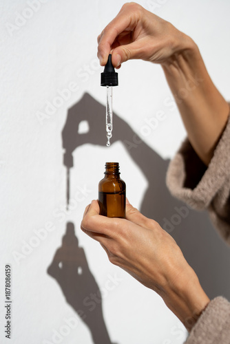 Fotografie Close-up of female hands holding glass dropper above amber cosmetic bottle, skin