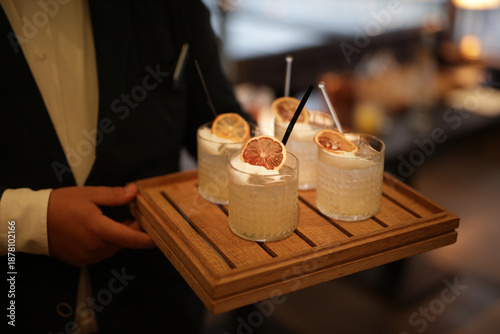 Obraz na plátně A waiter carries a wooden tray of elegant craft cocktails garnished with dried citrus and foam