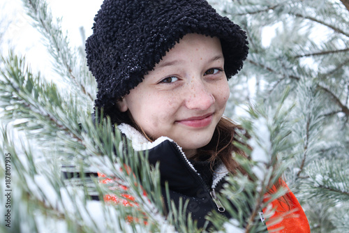 A thirteen-year-old girl in black stands among snow-covered pine branches during a winter walk