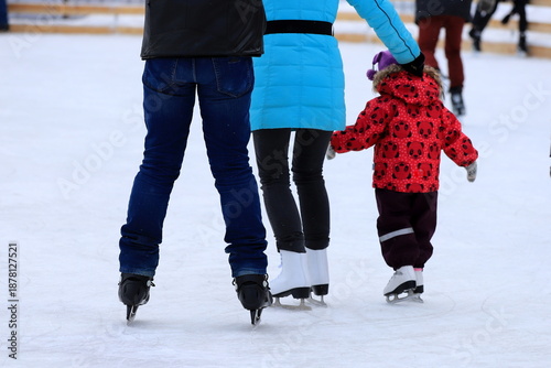 Little child skates at the ice rink in winter. A man and woman is teaching child to skate. Sports clubs, active family sport