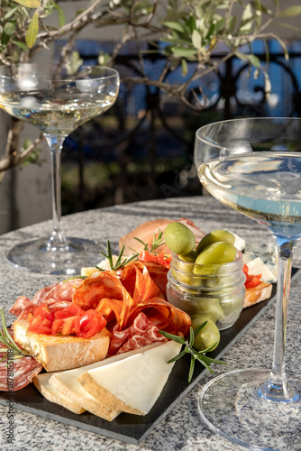 Outdoor Patio Gourmet charcuterie board with meats prosciutto ham, salami, green olives and cheese with white wine or prosecco aperitif or dinning outdoor Italian style