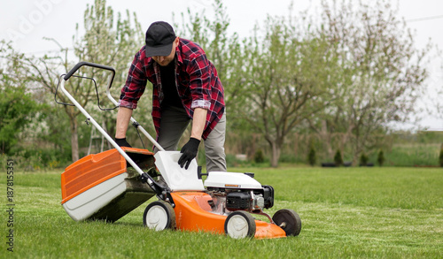Photos Man in casual clothes takes out bag with cut grass of lawn mower after mowing lawn with at own backyard
