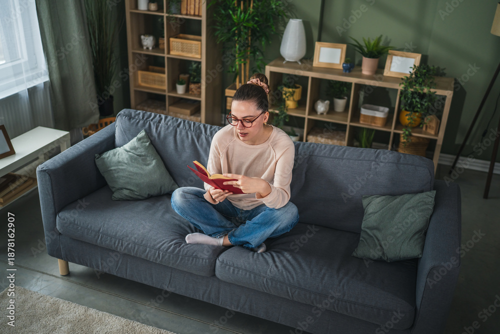 Obraz premium Young woman enjoying reading book on cozy sofa at home