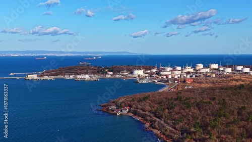 Wallpaper Mural A coastline features an industrial area with storage tanks and a few ships in the water under a bright sky. Trees line the shore, and the sea stretches into the distance. Torontodigital.ca
