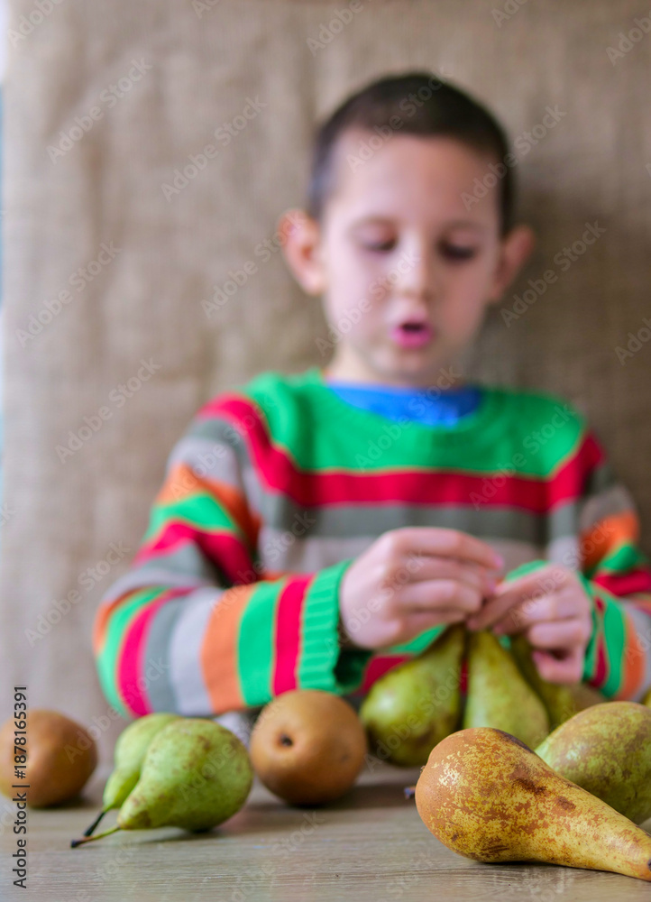 Fototapeta premium Young Boy Arranging a Variety of Fresh Pears on a Wooden Table
