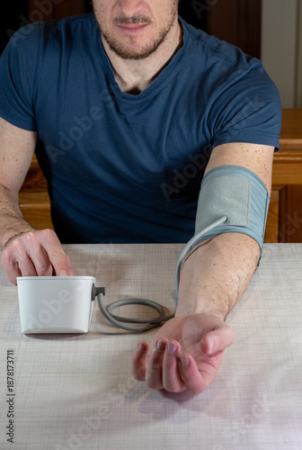 Man using a digital blood pressure monitor at home. Close up of a person sitting at a table with an automatic arm cuff for health monitoring, hypertension prevention and medical self-diagnostic.