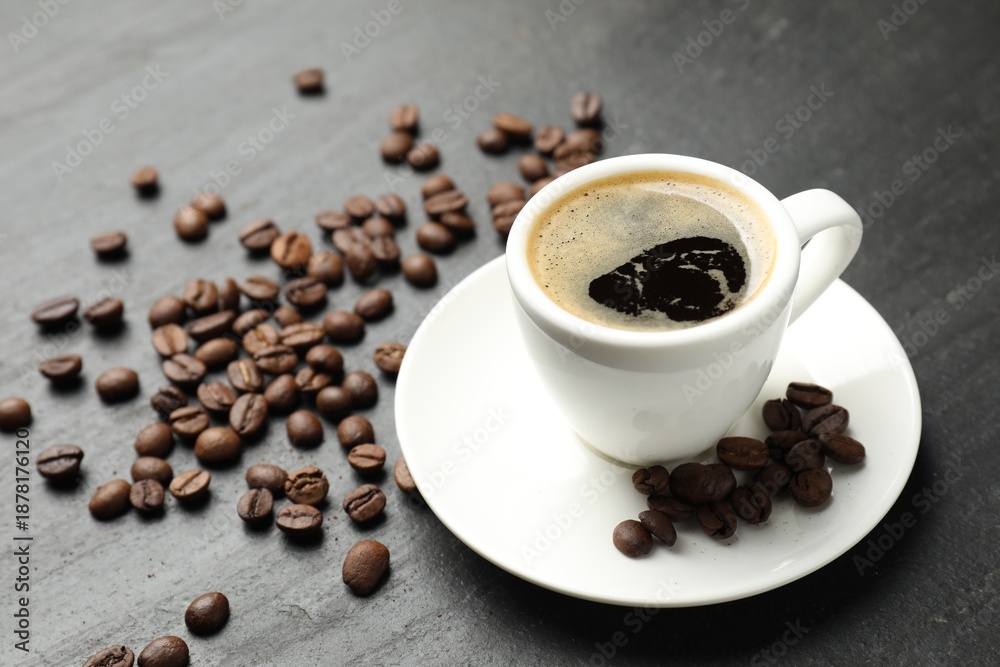 Obraz premium Refreshing coffee in cup and beans on dark textured table, closeup