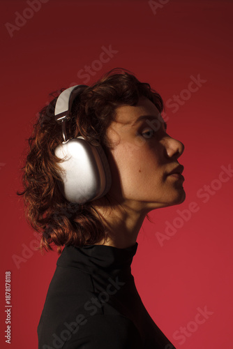 Profile portrait of a woman wearing headphones on red background. Music listening, focus, calm mood, lifestyle and audio concept.