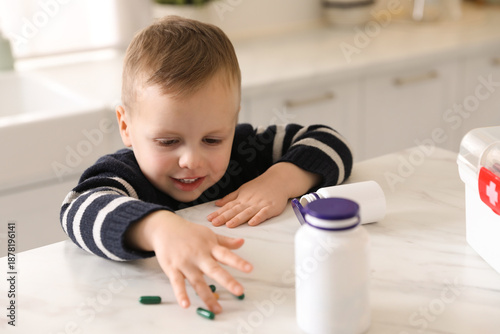 Child safety at home. Little boy playing with pills at table in kitchen