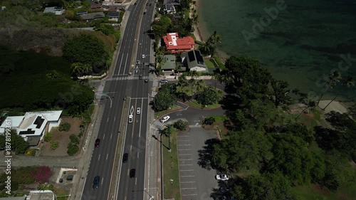 Aerial drone flying over coastal highway intersection beside tropical shoreline with palm trees and shallow ocean waters in Honolulu Hawaii
