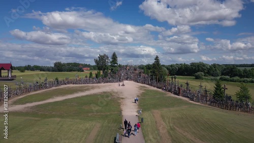 Hillside covered in countless crosses, with people walking on paths beneath a cloudy blue sky.