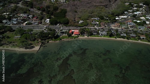 Aerial drone flying left along tropical coastline with shallow green water and residential neighborhood in Honolulu Hawaii
