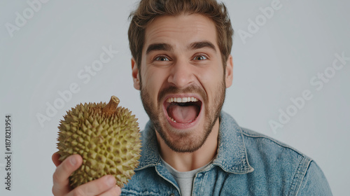 A joyful man excitedly holds a spiky durian fruit, showcasing his enthusiasm with a big smile against a light background.