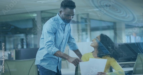 Pointing man in blue shirt leaning over woman in yellow top, showing document at modern office