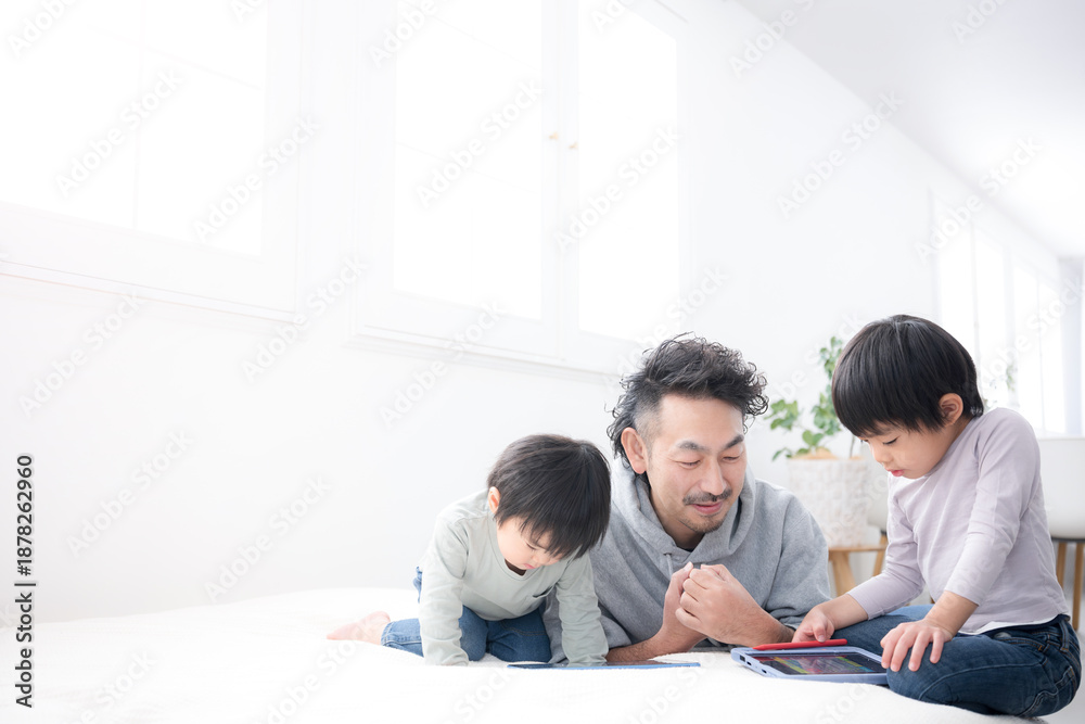 Fototapeta premium 親子でタブレットを使いながら一緒に勉強し遊びながら学ぶ休日の時間 父親と息子(兄弟)の楽しい育児 広角
