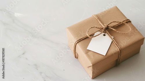 Minimalist kraft gift box with twine bow and blank tag. Birthday box on marble background.