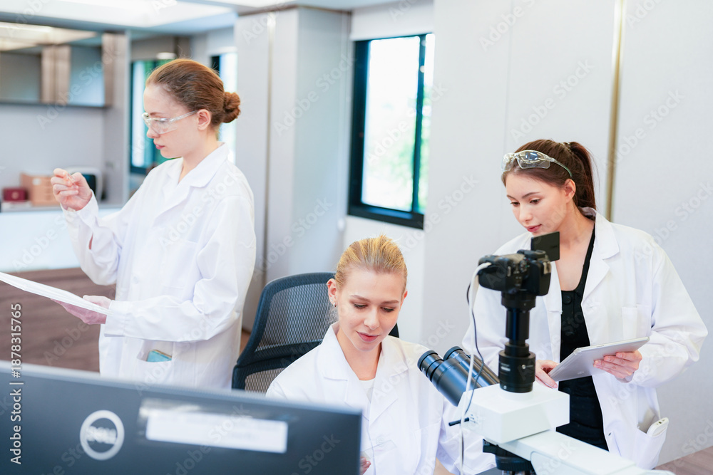 Obraz premium Asian female scientist using tablet to discuss histology results with colleague at microscope. Team collaborating on digital pathology analysis in modern lab.