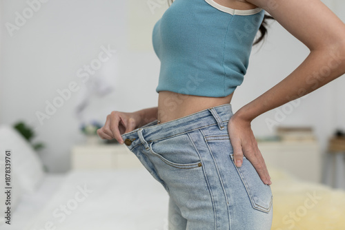 Tableau sur toile women wearing loose jeans after weight loss, holding waistband to show slimmer waist, concept of body transformation, diet success, fitness result, healthy lifestyle achievement