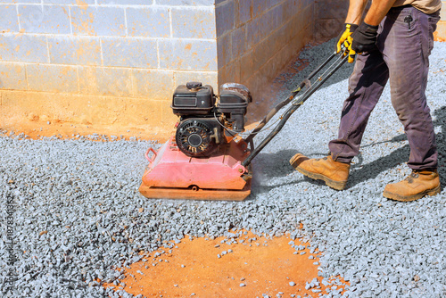 Worker uses compactor on gravel for construction site preparation