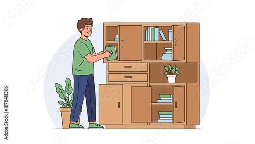 Young man in a green t shirt organizes his book collection in a large wooden cabinet with many shelves and cupboards.