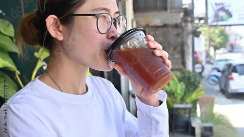 Asian woman drinking an iced Americano coffee. An iced americano is a refreshing coffee drink made with espresso and cold water, served over ice.