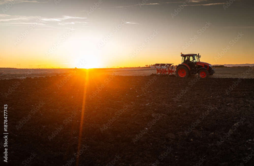 Fototapeta premium Tractor plowing field the land at sunset