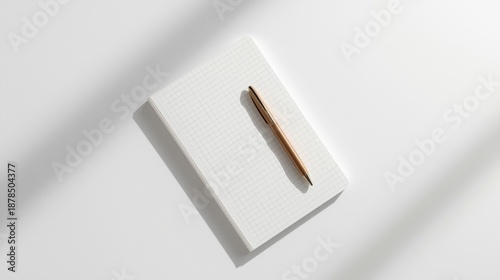 A gold pen on a minimalist white notebook with subtle grid pattern on a clean white background with soft shadows