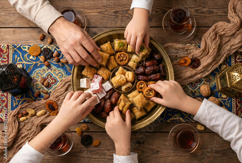 Top view of family hands reaching for traditional turkish sweets baklava dates and tea on a tray during ramadan iftar gathering