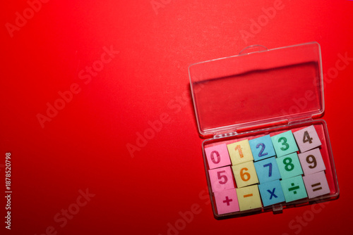 Colorful square tiles featuring numbers from 0 to 9 and mathematical symbols (plus, minus, multiplication, division, equals) are neatly arranged in a transparent plastic organizer.