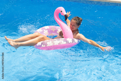 Happy woman floating on pink flamingo inflatable in pool