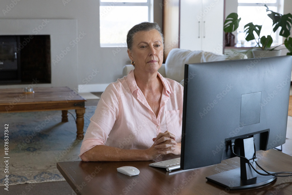 Fototapeta premium Senior woman wearing shirt working at living room desk using widescreen monitor and keyboard