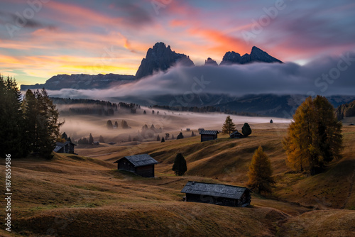 Iconic Seiser Alm landscape at dawn featuring traditional alpine huts and low-lying fog, South Tyrol.