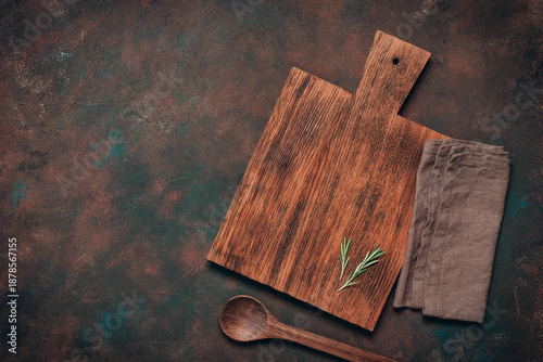 A culinary background with a wooden cutting board, wooden spoon, and linen napkin. Dark rusty grunge cooking backdrop. Top view, flat lay, copy space.