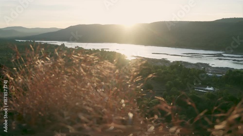 Panoramic view of a peaceful river valley during golden hour, featuring misty mountains and calm water at dawn