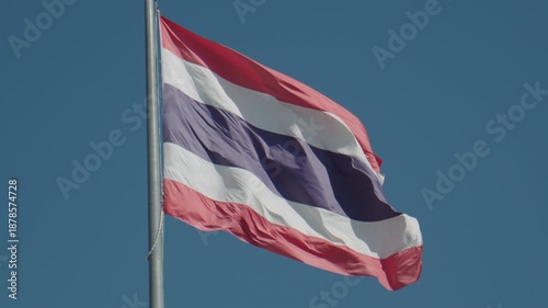 Thailand national flag waving on a pole against a clear blue sky, representing Thai identity and patriotism