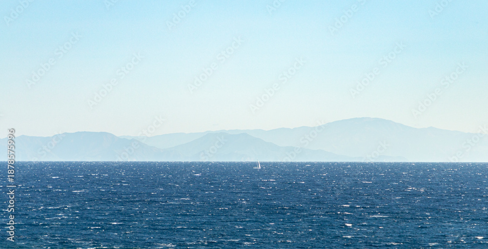 Fototapeta premium Vast blue ocean with distant mountains and sailboat 