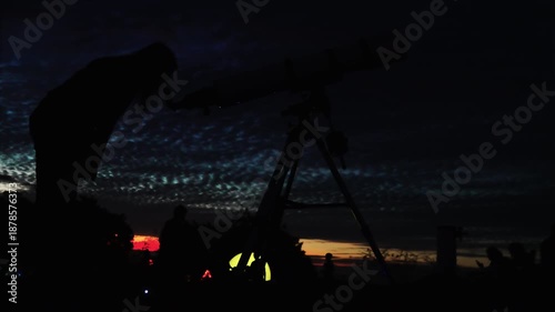 Silhouette of a person looking through a large professional telescope against a dramatic twilight sky for stargazing activity
