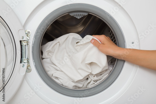 Young adult woman hands holding and unloading white sheet from opened washing machine. Clothes care. Closeup. Front view.