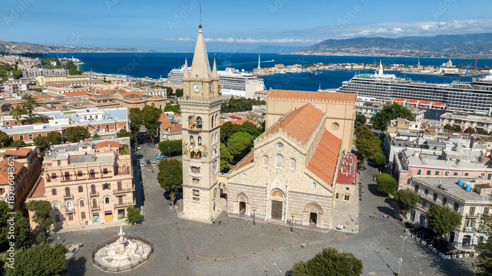 Fototapeta premium Aerial view of the Cathedral Basilica of Santa Maria, located in the historic center of Messina, Sicily, Italy. The Calabrian coast, separated by the Strait of Messina, is silhouetted on the horizon.
