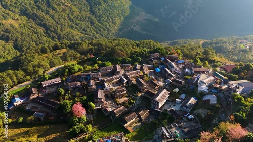 Aerial view of a village nestled in the mountains surrounded by lush green trees contrasting with the rustic rooftops, Himalaya, Annapurna, Nepal.