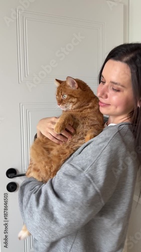 Girl brunette hugging and dancing with cute orange domestic cat at home