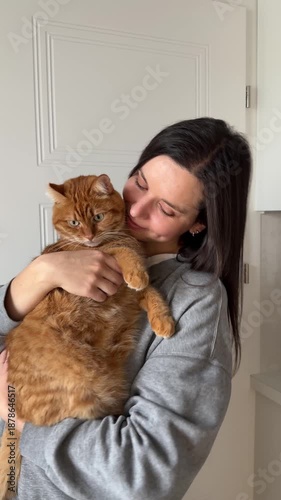Girl petting orange cat and dancing with him. Domestic ginger cat sitting in hands of his owner at home.