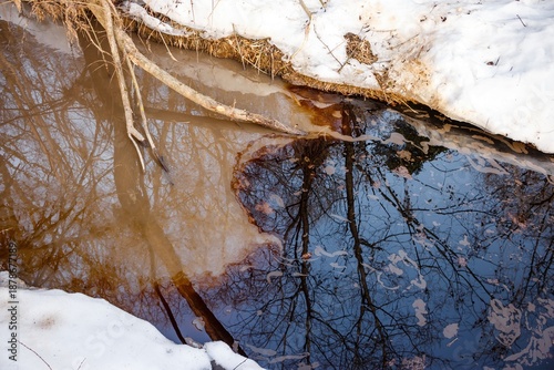 Obraz na plátně Foul oil spill contaminates a peaceful winter creek, its iridescent sheen marring the clear reflections of bare trees