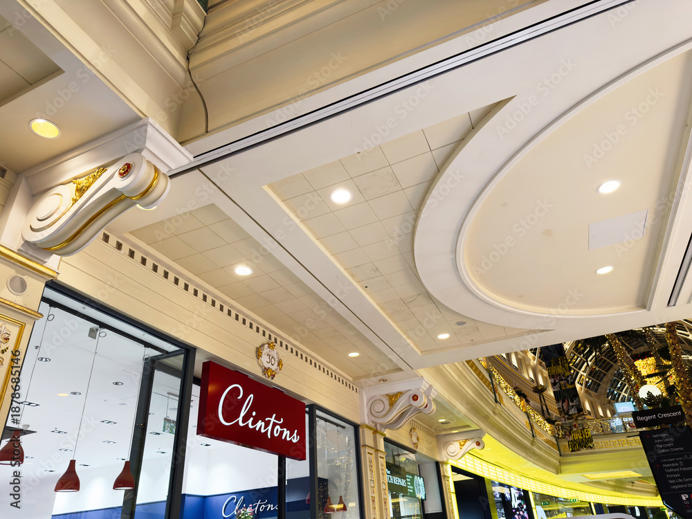 Naklejka premium Elegant Manchester shopping mall interior with ornate ceiling and Clintons storefront display in a luxury retail setting
