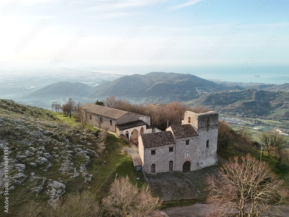 Fototapeta premium Abbey of Maria Santissima on Mount Tubenna with panoramic views.Immersed in a picturesque mountain landscape, the historic stone complex stands out on the ridge with the hills and coast visible