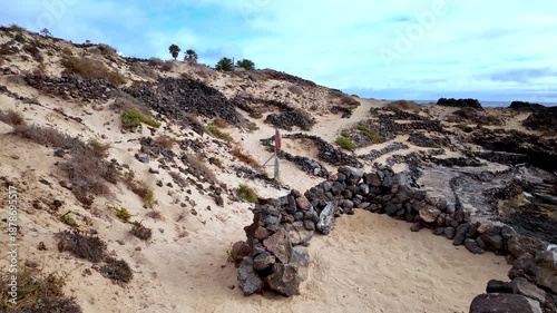 Unique volcanic landscape in Charco del Palo, Lanzarote, featuring sandy paths and natural pools formed by lava rocks next to the Atlantic Ocean on a serene, cloudy day